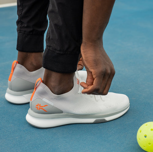 Man lacing his shoes up on a pickle ball court