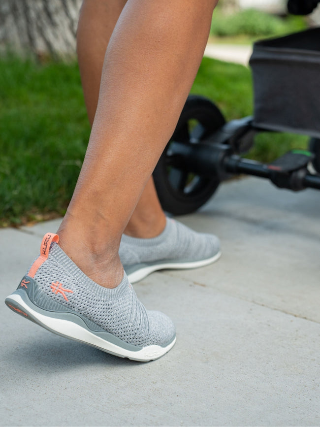 The feet of a woman walking with a stroller while wearing STRIDE Women's Slip-on Sneaker in HeatherGray-White-PeachPink