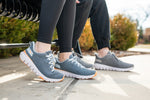Two people sitting on a bench in profile, with a detailed view of their shoes wearing two different variants of FLEX Via sneakers by KURU Footwear