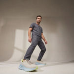 Man wearing a gray outfit with light blue and green sneakers on a neutral background