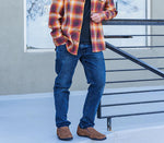 Man stands at the top of some stairs leaning on the railing wearing KURU Footwear's KIVI in the color ChestnutBrown 