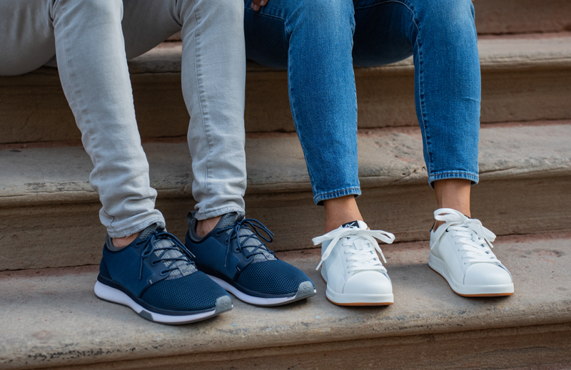 Two people sitting on stair steps, showcasing two different styles of shoes by KURU Footwear.