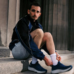 Man sitting on steps lacing KURU ATOM 2 Slip-On Men's Sneaker in Mountain Blue-Dove Gray.