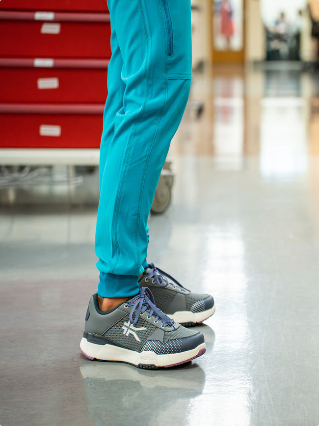 Healthcare worker standing on a hospital floor wearing gray KURU athletic sneakers for all-day support.