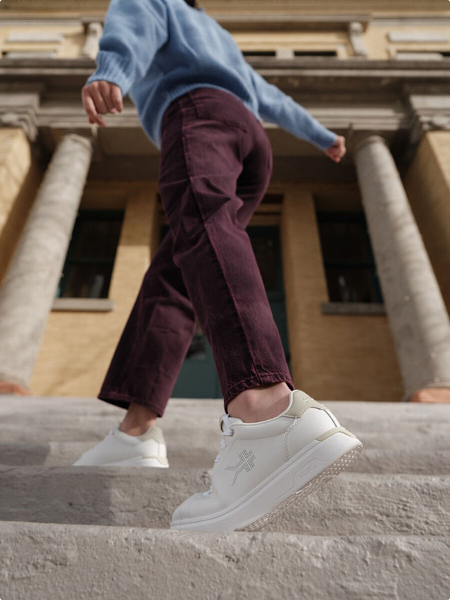 Person stepping up stone stairs wearing white KURU walking sneakers with logo detail.