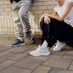 Two people wearing KURU DASH Vanta unisex sneakers in Bright White on a city sidewalk.