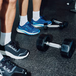 Person standing among dumbbells in KURU DASH Vanta unisex sneakers in Indigo Blue.