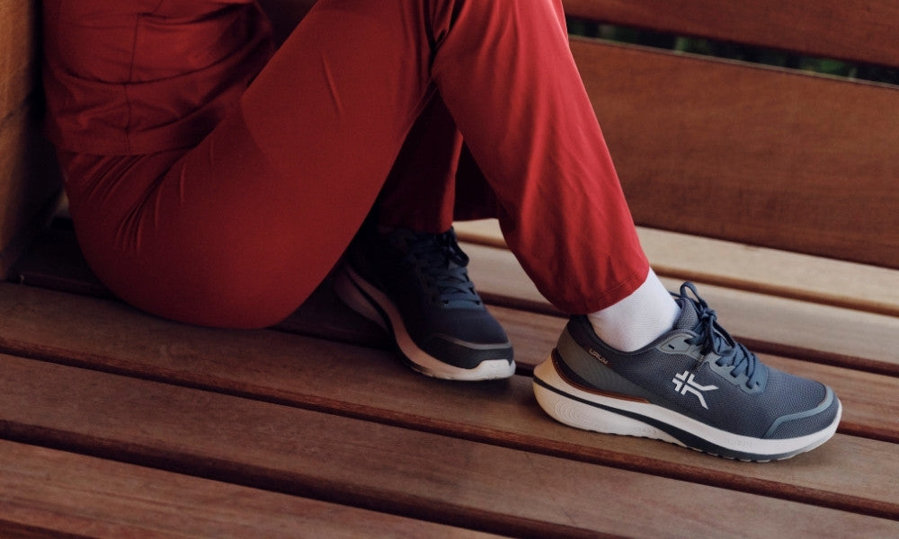 Person resting on a bench wearing KURU DASH Vanta sneakers for all-day comfort and heel pain relief.