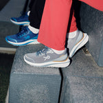Person wearing KURU DASH Vanta unisex sneakers in Steel Grey-Tan while sitting on outdoor steps.
