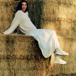 Woman seated on hay bales wearing KURU DRAFT 2 Women's Cozy Clogs in Winter Cream-Ashwood.