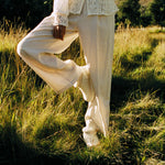 Woman standing in tall grass wearing KURU DRAFT Lahti Women's Cozy Boots in Winter Cream-Ashwood at golden hour.