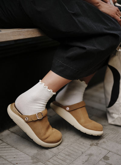Woman sitting on a bench wearing KURU clogs in Tan with cushioned support for all-day comfort.