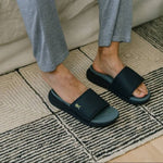 Feet at home wearing KURU MOMENT Men's Slide Sandal in Midnight Blue-Pale Lime.