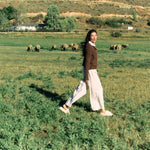 Woman walking through a green pasture wearing KURU MOMENT Women's Cozy sandals in Winter Cream-Ashwood.