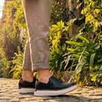 Woman wearing KURU ROAM 2 Atla Women's Slip-On in Jet Black-Cognac Brown on a garden path.