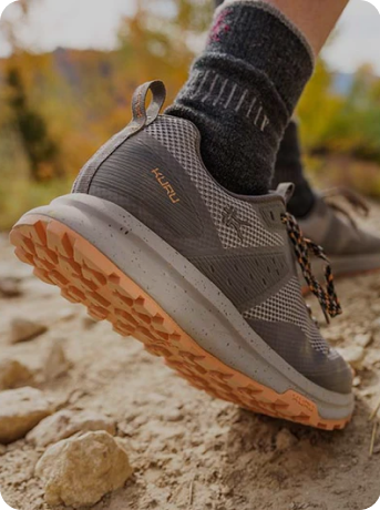 A person's feet on a rocky trail and wearing ATOM Trail.