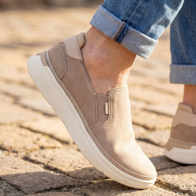 Beige slip-on shoes worn with rolled-up jeans on a stone pavement.