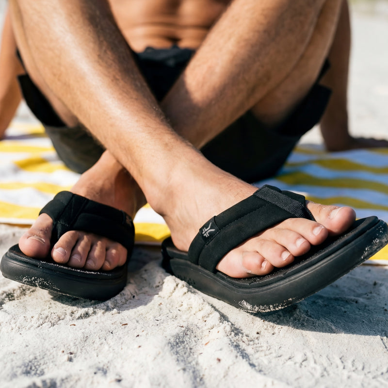 Person wearing black sandals on a sandy surface