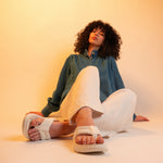 Woman sitting on a white surface wearing white sandals against a beige background
