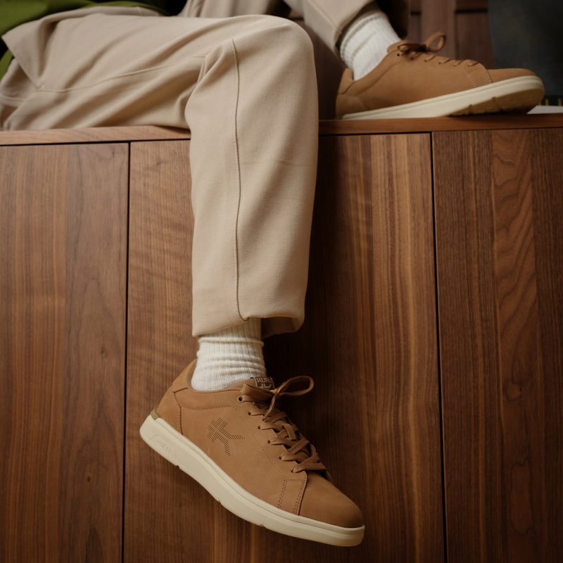 Person wearing brown shoes and beige pants sitting on a wooden surface.