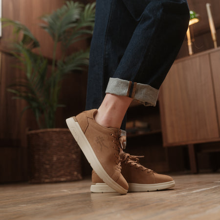 Person wearing brown shoes with white soles indoors, with plants and furniture in the background.