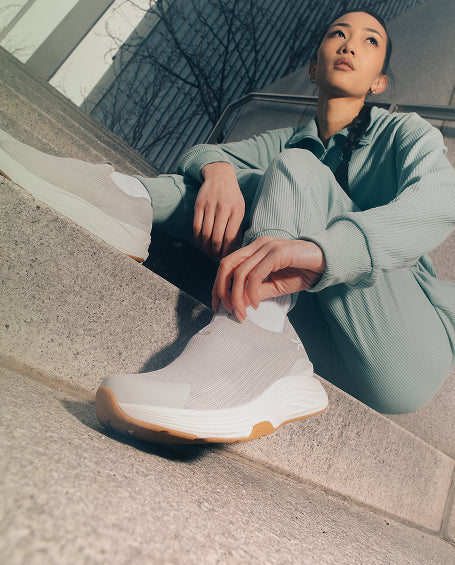 Person sitting on steps wearing light-colored sneakers with a neutral background