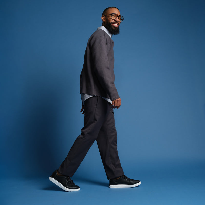 Man walking in a gray suit and black shoes on a blue background