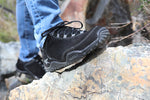 Man wearing KURU Footwear's CHICANE Men's Trail Hiking Shoe in SmokestackBlack hiking over rocks.