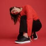 Woman wearing a red sweater and black pants on a red background